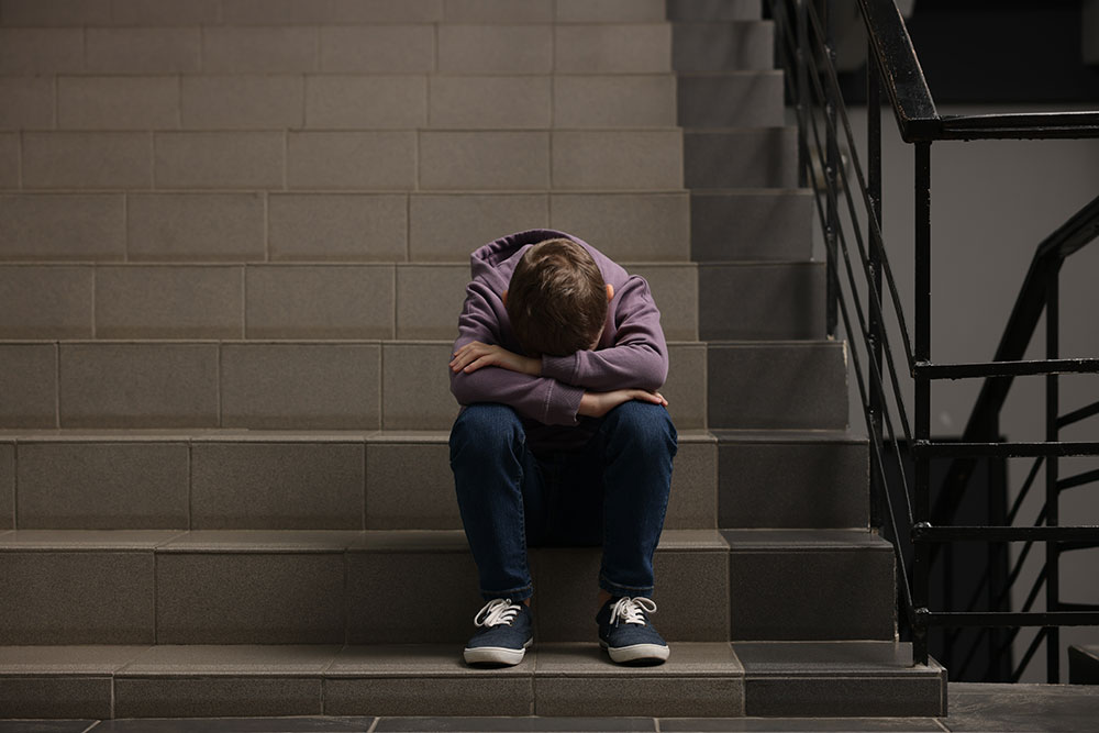 Child Sex Abuse Definition and Meaning young boy sitting on stairs with head in hands